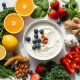 Bowl of yogurt topped with blueberries and almonds surrounded by citrus berries greens ginger garlic and peppers on a marble surface healthy food collage