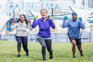 Group of diverse adults running toward the camera each holding small dumbbells during an outdoor workout in a park