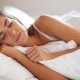 Woman sleeping peacefully on white pillows and bedding with eyes closed lying on her side in bed
